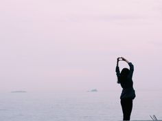 a woman standing on top of a beach next to the ocean holding her hands up