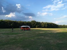 two people standing in the grass next to a red and white tent under a cloudy blue sky