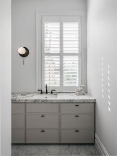 a bathroom with marble counter tops and white shutters on the window sill above it