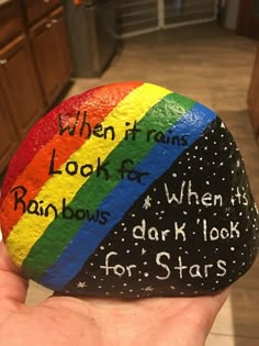 a hand holding a rock with writing on it that says when it rains, look for rainbows