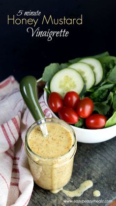 a jar filled with dressing next to a bowl full of vegetables and cucumbers