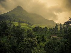 the mountains are covered in green trees and bushes as clouds hover over them on a cloudy day