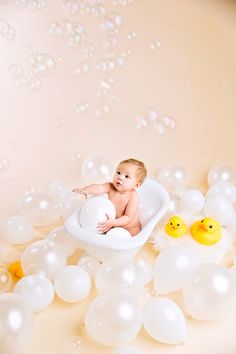 a baby in a bathtub surrounded by balloons and rubber ducks