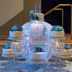 an elaborately decorated wedding cake with blue flowers and candles on a cart in front of stairs