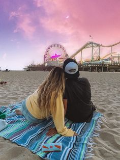 two people sitting on a blanket at the beach with a ferris wheel in the background