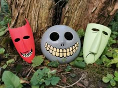 three halloween masks sitting next to a tree