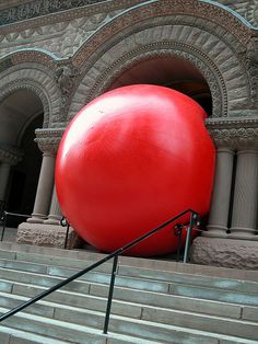 a large red ball sitting on top of a set of stairs in front of a building