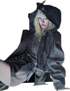 a woman in a black jacket and hoodie sitting on the ground with her legs crossed