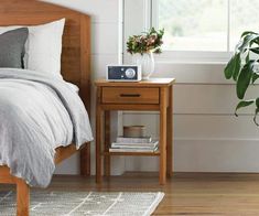 a bedroom with a bed, nightstand and plant on the side table next to it