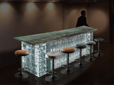 a man standing at a bar with four stools in front of it and the counter is made out of glass blocks