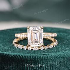 an emerald colored diamond engagement ring set on top of a green velvet cushioned pillow