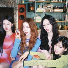 four young women sitting on a couch in front of a fireplace with bookshelves behind them