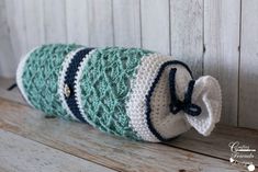 a crocheted tube is sitting on a wooden shelf with a bow tie around it