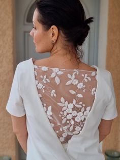 a woman wearing a white top with flowers on it's back, standing in front of a door