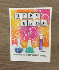 a happy birthday card with some science themed items in the background on a wooden table