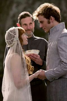 a man and woman standing next to each other in front of a stone wall wearing wedding veils