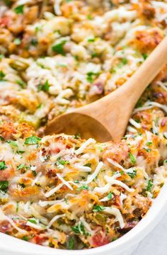 a casserole dish with meat, cheese and vegetables in it has a wooden spoon