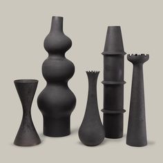 several black vases are lined up on a white surface, one is tall and the other is short