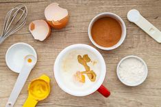 an assortment of ingredients including eggs, flour and other items on a wooden table with measuring spoons