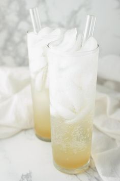 two glasses filled with ice sitting on top of a marble counter next to each other