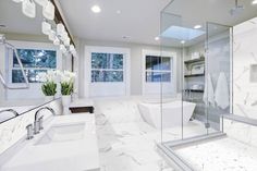 a large bathroom with white marble counter tops and floor to ceiling glass shower doors, two sinks on either side of the bathtub