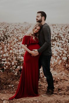 a pregnant couple standing in the middle of a cotton field