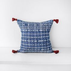 a blue and white pillow with tassels on the front, sitting on a shelf