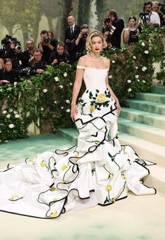 a woman in a white dress standing on some steps with people taking pictures behind her