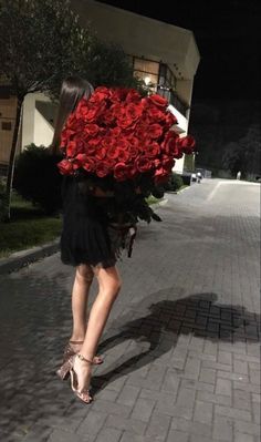 a woman walking down the street carrying a large bunch of red roses