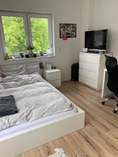 a bedroom with a bed, desk and television on the wall in front of two windows