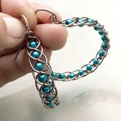 a person holding a piece of metal with blue beads on it's end and an open loop around the clasp