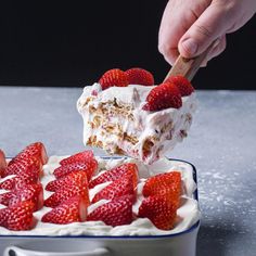 someone scooping strawberries out of a cake with white frosting in a blue and white dish