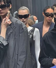 a group of people standing next to each other in front of a mirror wearing sunglasses