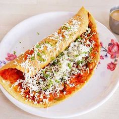 a piece of bread with cheese and sauce on it sitting on a plate next to a cup