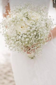 a bride holding a bouquet of baby's breath in her hand on the beach