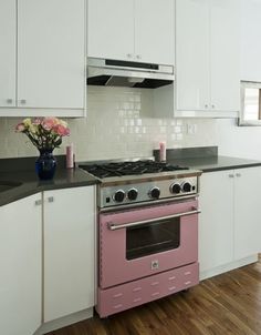 a pink stove top oven sitting inside of a kitchen next to white cabinets and wooden floors