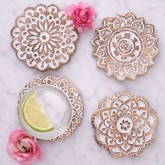 four decorative coasters on a marble table with pink flowers and a lime slice next to them