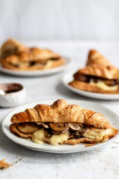 croissant sandwich with mushrooms and brie on white plate next to other pastries