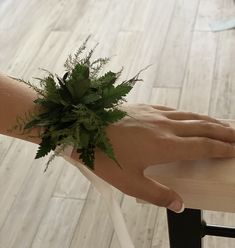 a person's hand with a green plant on top of their left arm, sitting at a table