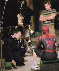 two men sitting on stools in front of a spider - man suit and camera