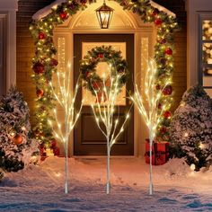 christmas lights decorate the front door of a house with wreaths and trees in the snow