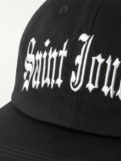 The LA streetwear scene is obsessed with Old English lettering – it's been blasted across baseball caps since the early '90s. Tapping co-founder Cali Thornhill Dewitt's SoCal roots, SAINT Mxxxxxx's trucker hat is made from cotton-twill and embroidered with 'Saint Journey' in the script. Classic Hats With Logo Print For Streetwear, Classic Logo Print Hat For Streetwear, Vintage Dad Hat For Streetwear And Baseball Season, Black Letter Print Dad Hat For Streetwear, Vintage Baseball Cap With Embroidered Logo For Streetwear, Black Dad Hat With Letter Print For Streetwear, Black Logo Print Baseball Cap For Streetwear, Streetwear Fitted Hat With Logo Patch For Baseball Season, Streetwear Flat Brim Fitted Hat With Logo Patch