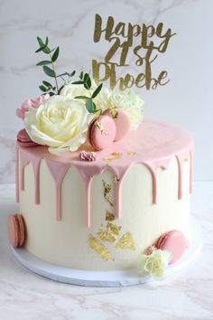 a birthday cake decorated with pink and white icing, flowers and gold leaf decorations