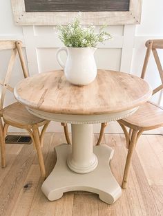 a white vase sitting on top of a wooden table next to two chairs and a chalkboard