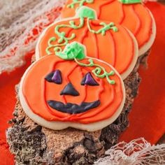 three decorated halloween cookies sitting on top of a tree stump next to a red cloth