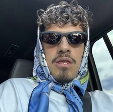 a man wearing sunglasses and a scarf in the back seat of a car with his head covered by a bandana