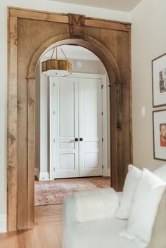 an archway leading into a living room with white furniture and framed pictures on the wall