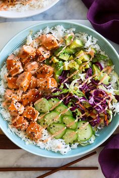 two bowls filled with rice, cucumber, and salmon next to chopsticks