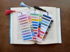 three bookmarks with different colors on them sitting on top of an open book next to a tassel