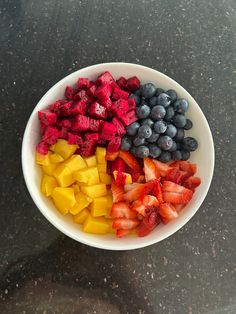 a white bowl filled with fruit on top of a black counter topped with blueberries, strawberries and mangoes